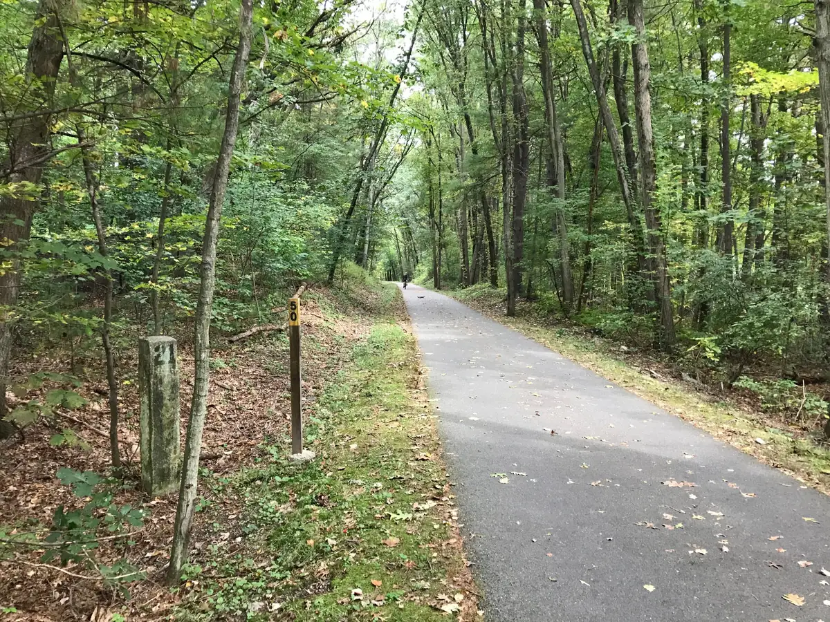 Paved Bruce Freeman Rail Trail through the woods in Chelmsford, MA, with a mile marker post